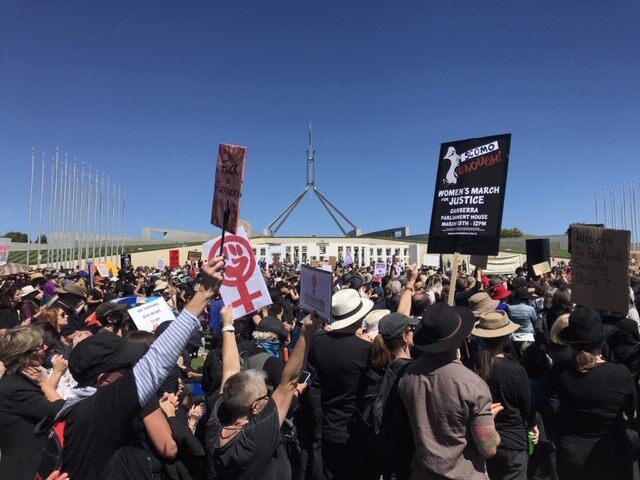 Hundreds of protesters gathered outside Parliament House in Canberra holding signs.