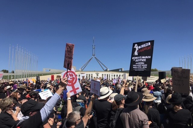 Hundreds of protesters gathered outside Parliament House in Canberra holding signs.