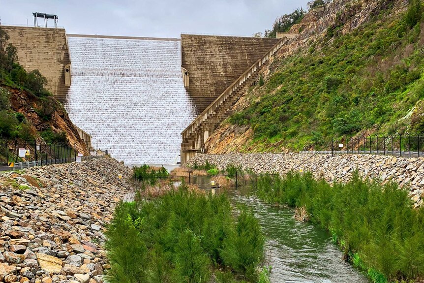 Water spills down a dam wall to river a below.