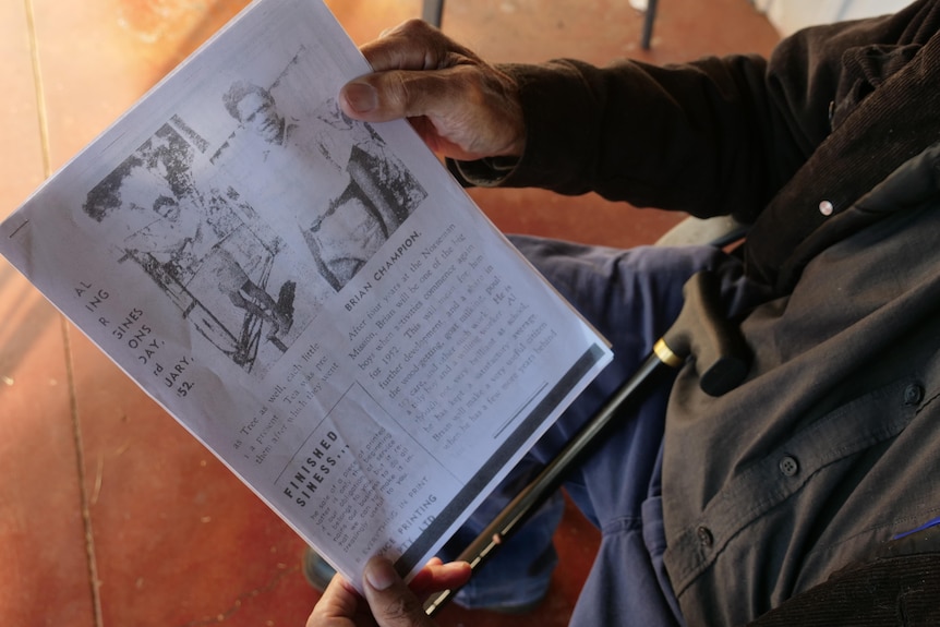 Man holds photocopy of old newspaper page.