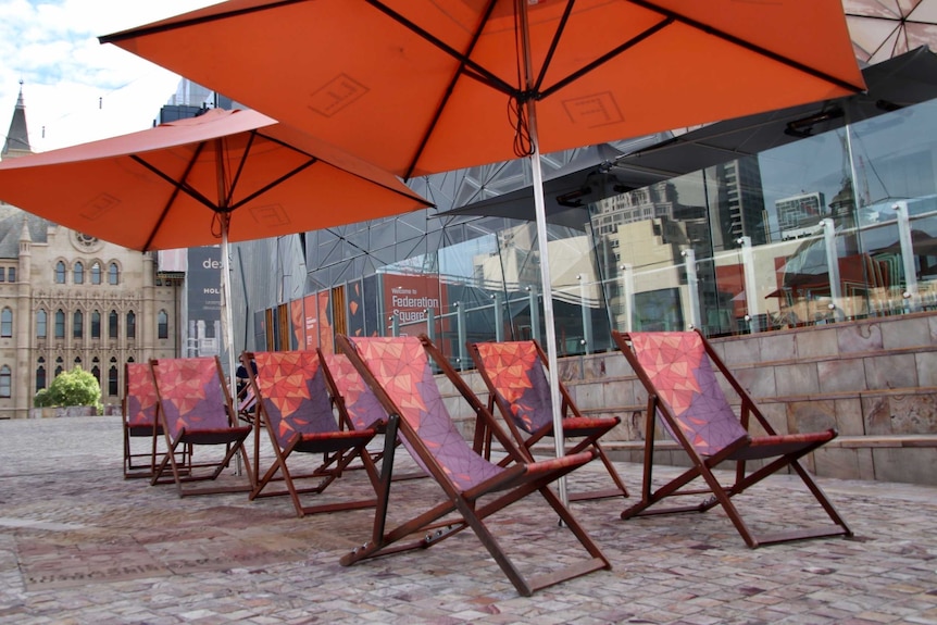 Empty lawn chairs under market umbrellas at Federation Square.