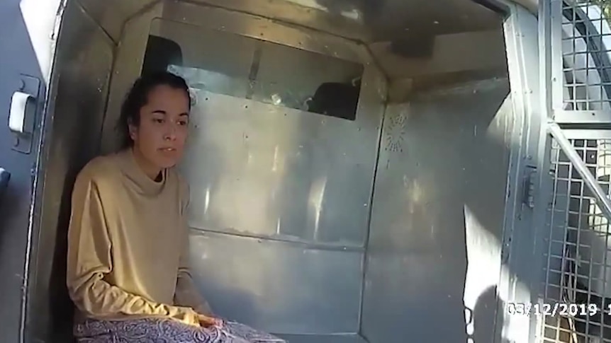 A woman sits in the back of a police wagon.