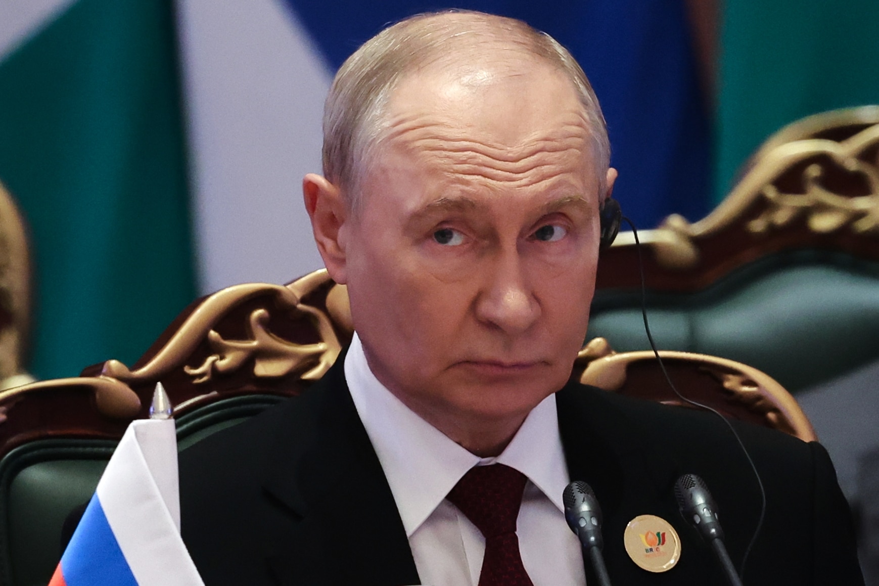 A headshot of Vladimir Putin wearing a white shirt and black vest.