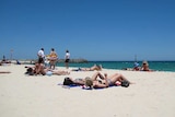 A wide panoramic shot of people sunbathing and swimming on Cottesloe beach in Perth under a bright blue sky.
