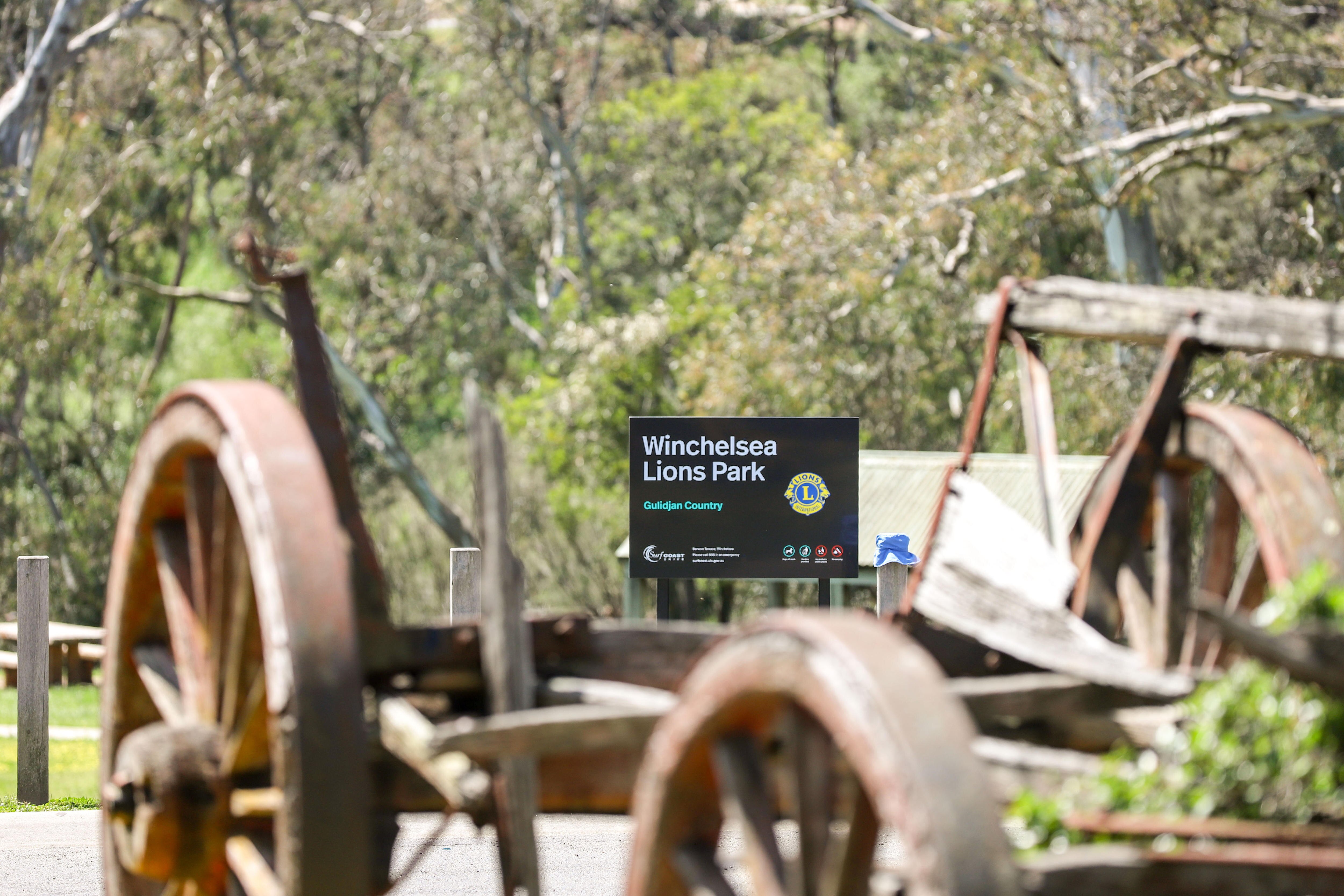 A sign in a leafy green park in Winchelsea visible through an old broken down cart
