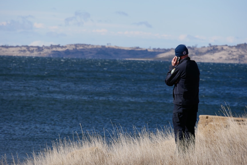 A police officer on the phone looks out over a lake