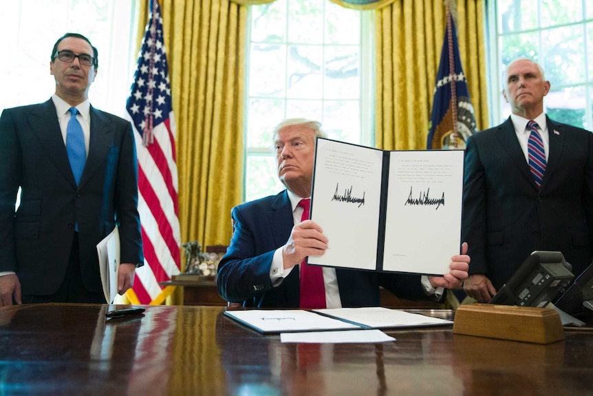 President Donald Trump holds up a signed executive order as two men stand either side of his desk.