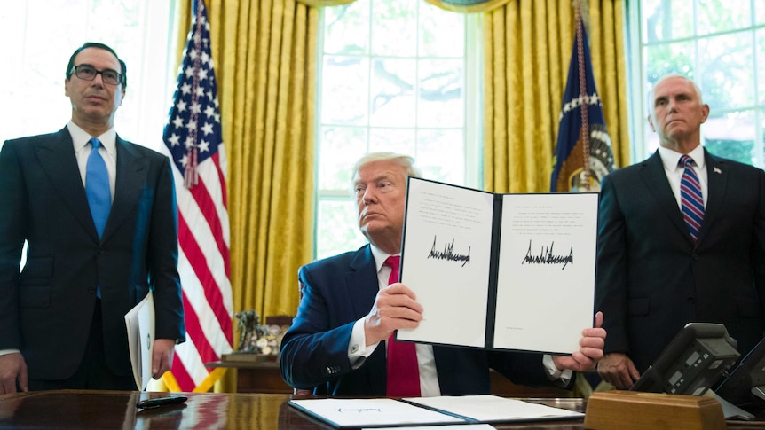 President Donald Trump holds up a signed executive order as two men stand either side of his desk.