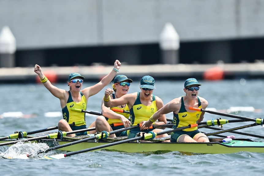 Four women in a boat raise their arms in the air