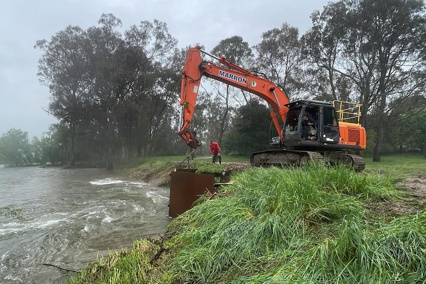 A machine helping to clear an eroded river levee bank with a person next to it