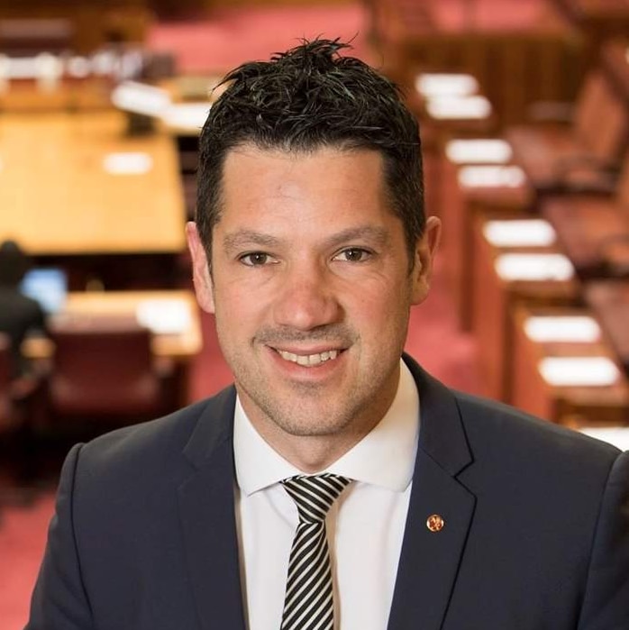A man with dark brown hair wearing a suit in front of the Senate chamber