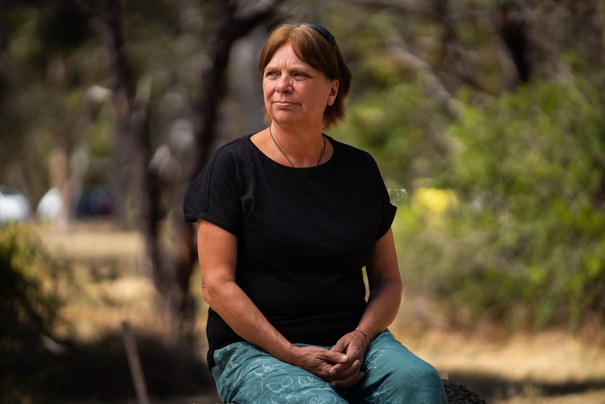 Fiona Pettiford sitting on a chair in a park, with her hands clasped, looking pensive.