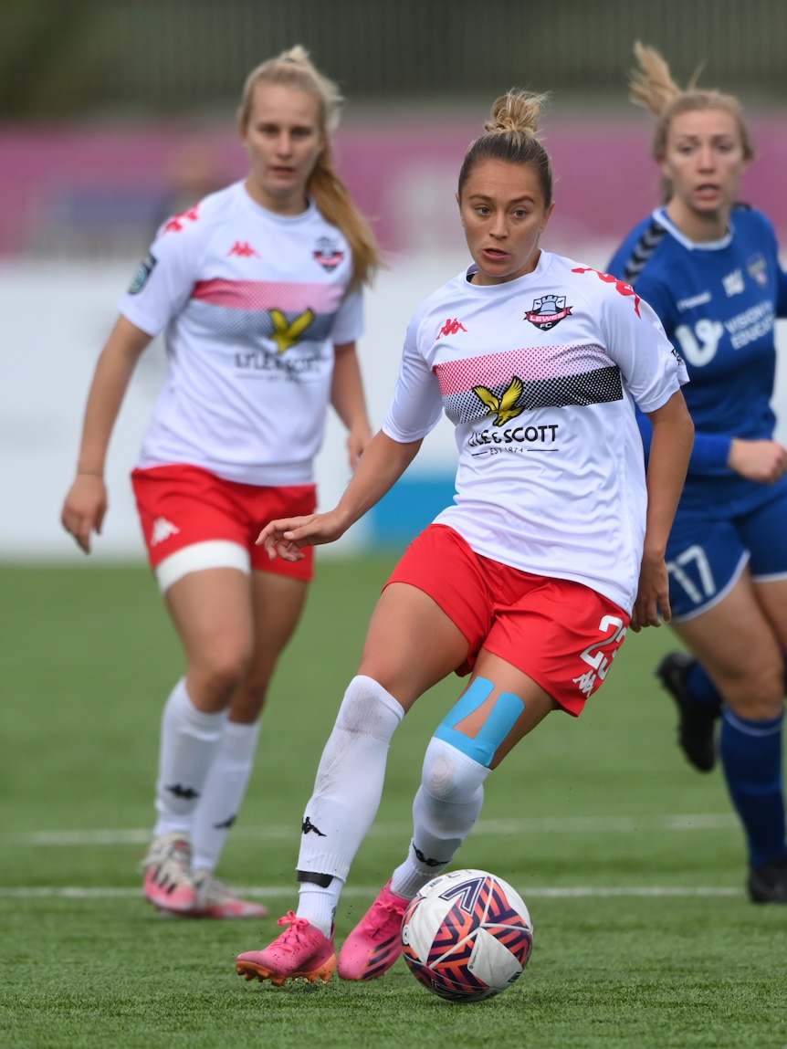 A soccer player wearing white, red and black kicks the ball on the grass during a game