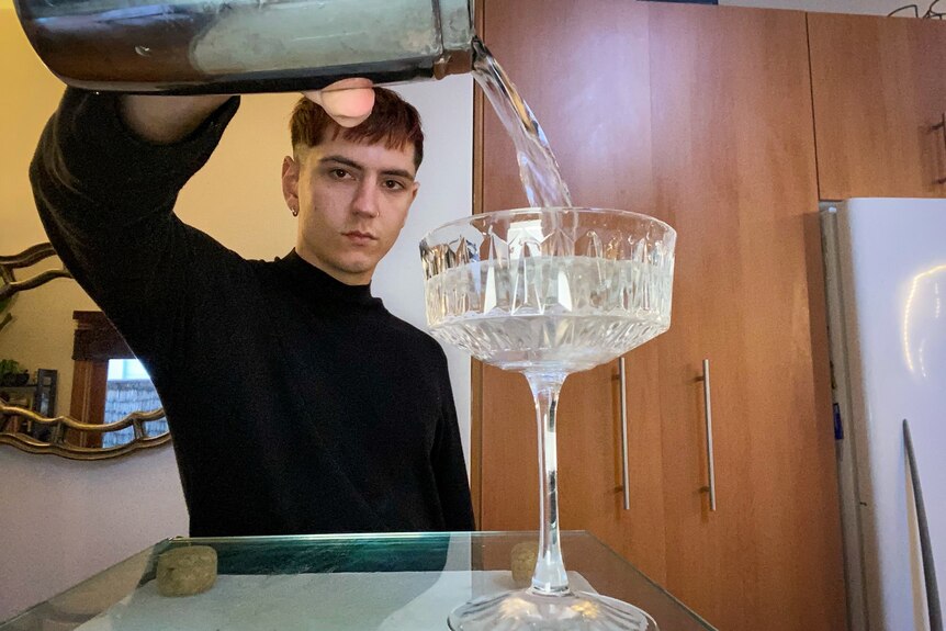 A young man dressed in black pours a cocktail into a crystal glass