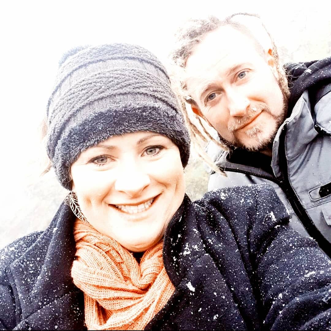 A man and a woman smiling at the camera with snow on their clothes.