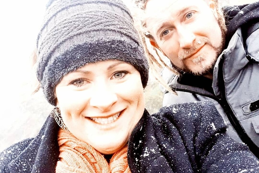 A man and a woman smiling at the camera with snow on their clothes.