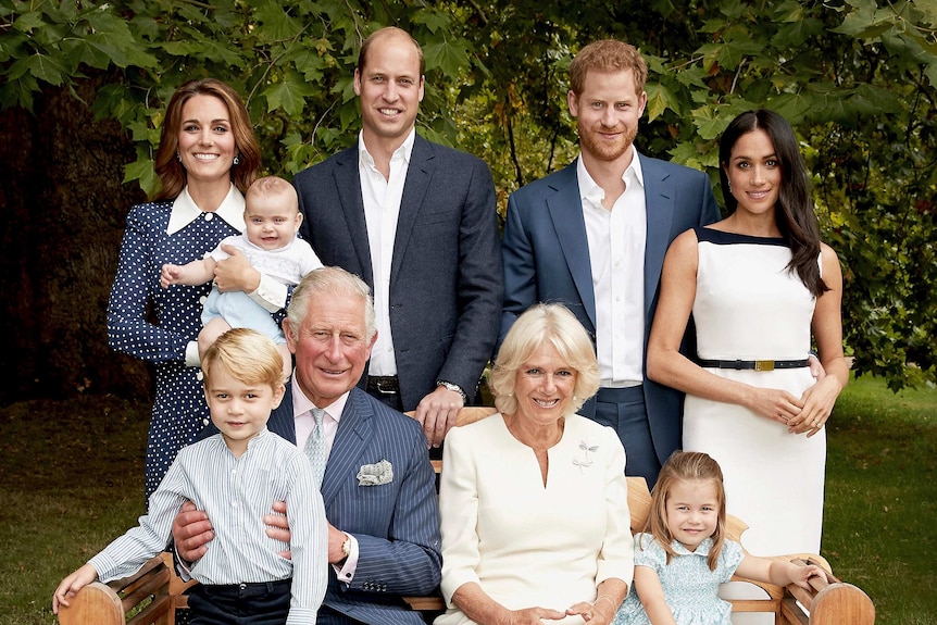 Prince Charles sits on a garden bench with grandson George on his knee, surrounded by his wife, sons and their families, smiling