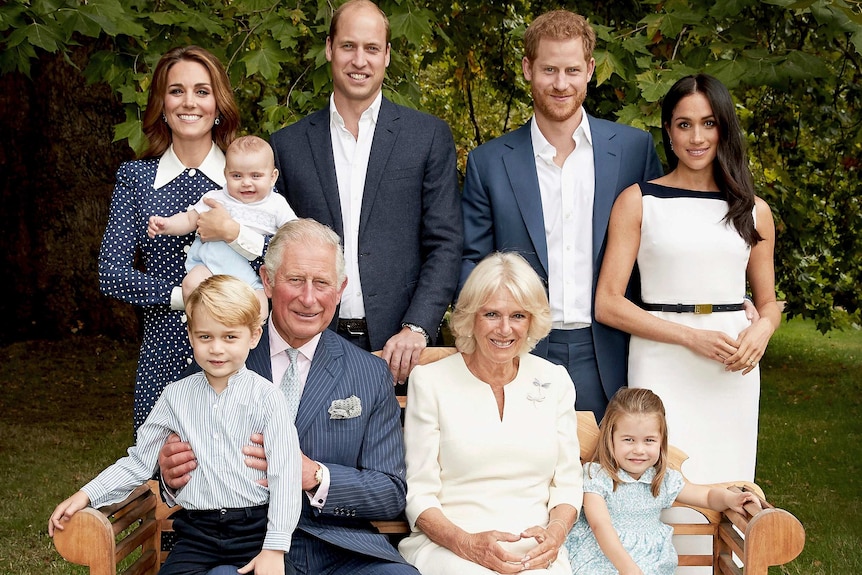 Prince Charles sits on a garden bench with grandson George on his knee, surrounded by his wife, sons and their families, smiling