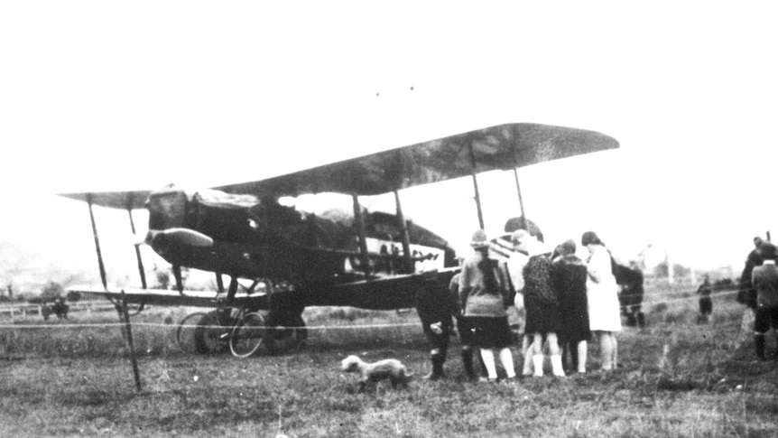 A crowd of people gather around an old bi-plane.