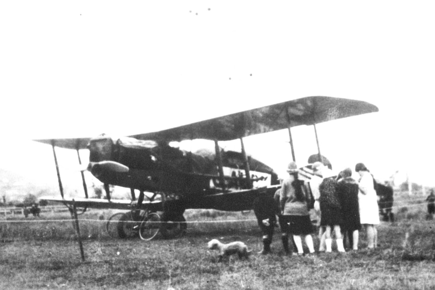A crowd of people gather around an old biplane.