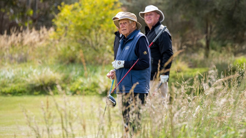 Three men holding golf clubs stand in a field