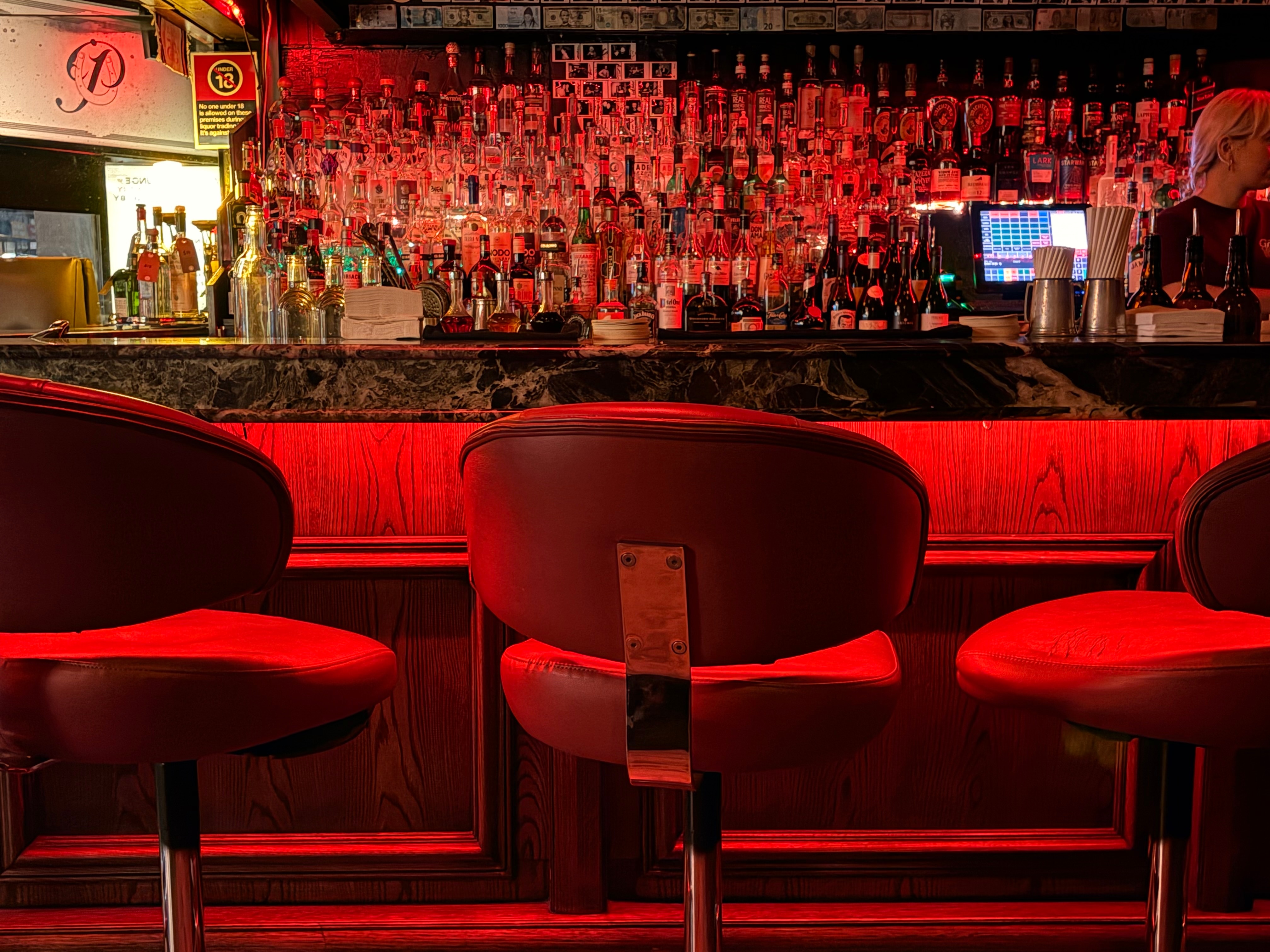 Bottles behind the bar , illuminated by red light. Empty bar stools in foreground
