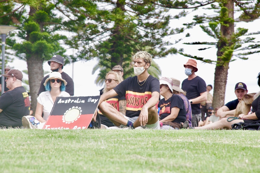 A man sitting on the ground wearing a mask and T-shirt that reads "Always was".