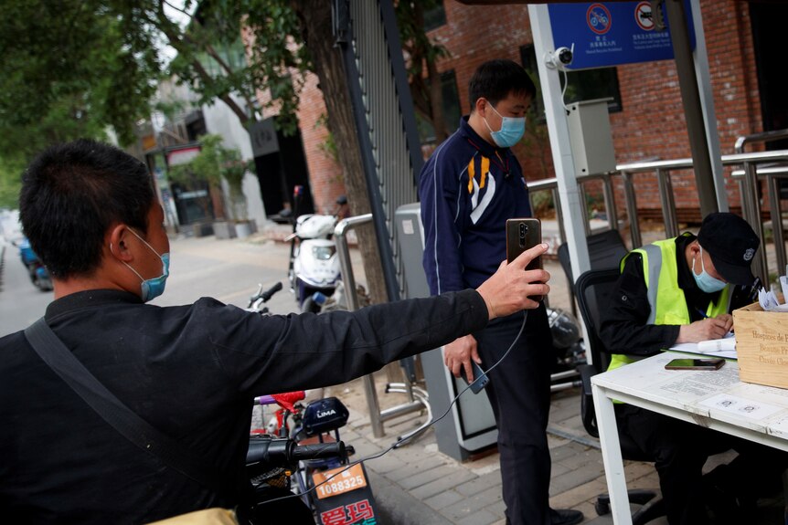 A delivery driver holds up his smartphone to present the status of his health app to security at a checkpoint.