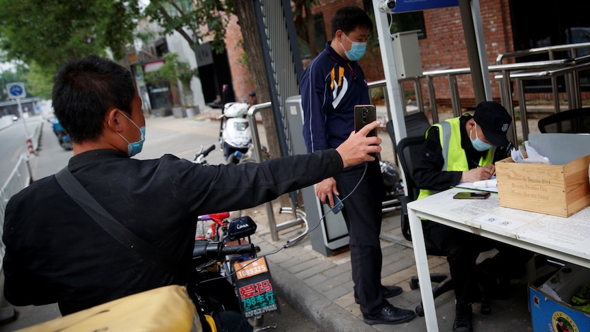 A delivery driver holds up his smartphone to present the status of his health app to security at a checkpoint.