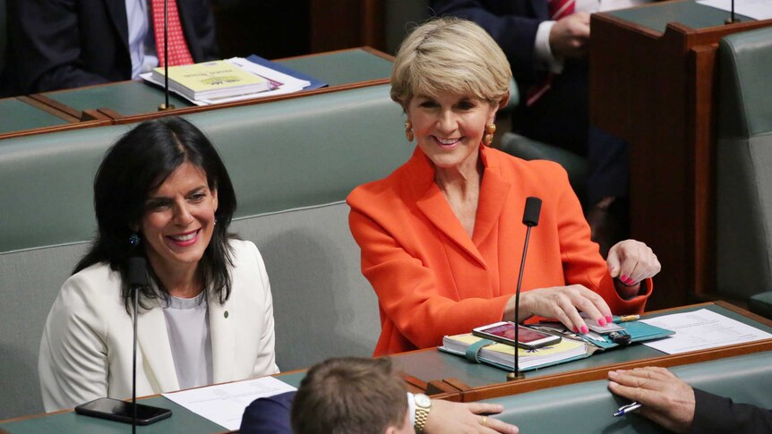 Julia Banks, wearing a white jacket and grey top, sits next to Julie Bishop resplendent in orange. Both women are smiling.
