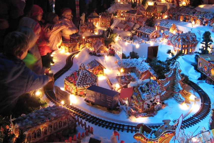 People look at a model railway line running in a large corner around model homes and buildings made from gingerbread.