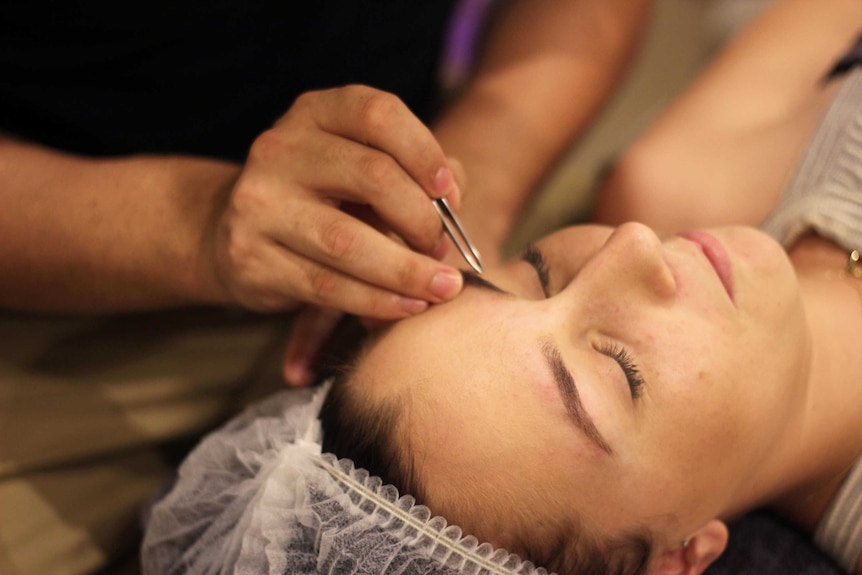 A man's hands plucking a woman's eyebrows.