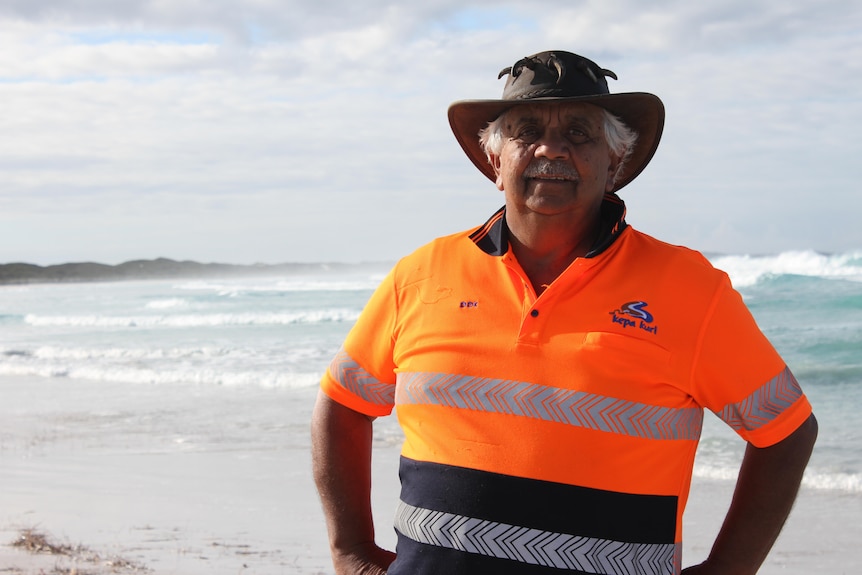 A man stands on the beach wearing a fluro shirt and hat.