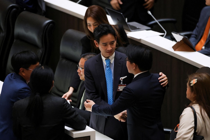 Pita Limjaroenrat wears a dark suit as he shakes hands with other politicians in parliament. 