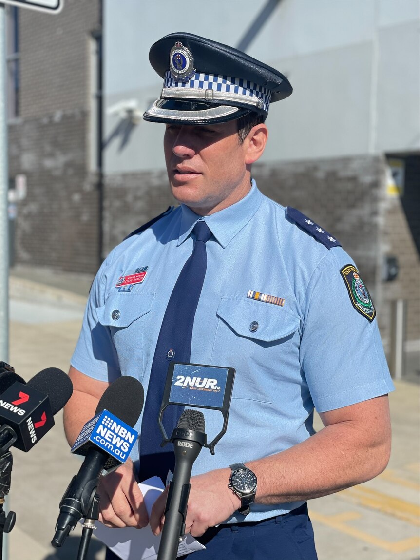 A police officer in uniform addressing the media in front of several microphones.