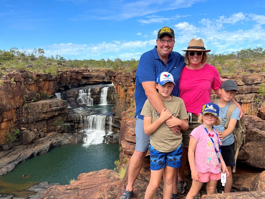 A family of five standing in front of a waterfall in the outback. 