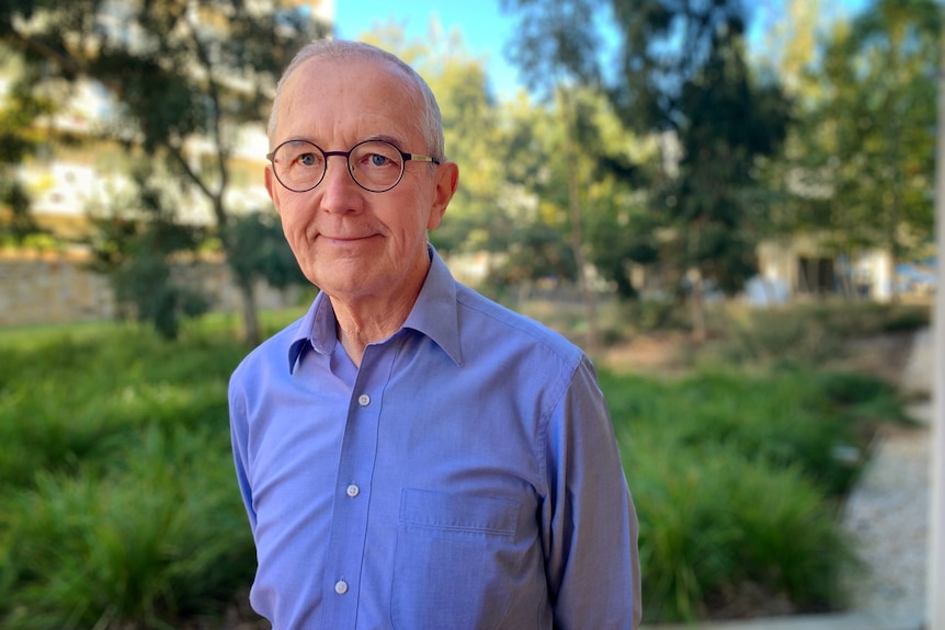 A man with grey hair and glasses wearing a blue shirt smiles for the camera 