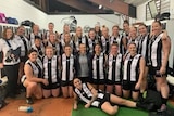 A group of women wearing black and white stripped AFL uniforms poses for a photo in the change rooms