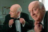 John Clarke adjusting a bow tie in front of a mirror.