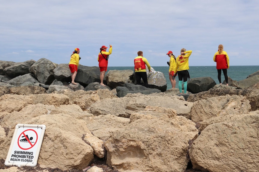 Surf lifesavers stand on rocks at Pyramids Beach urging people to get out of the water.