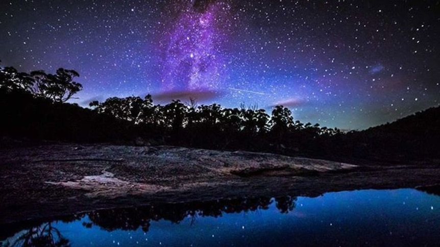 The Milky Way and stars  reflected in a lake, with trees on the horizon, at Girraween National Park in NSW.