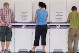 Three people stand in front of a row of voting booths.