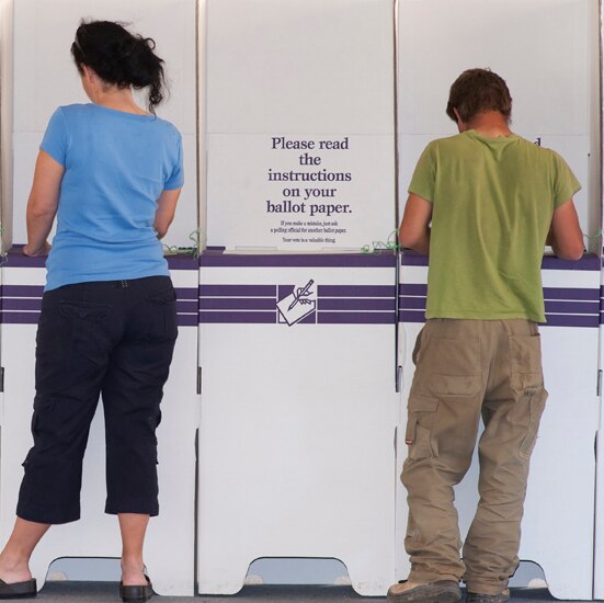 Two men and a woman standing at ballot boxes filling in their ballot papers.