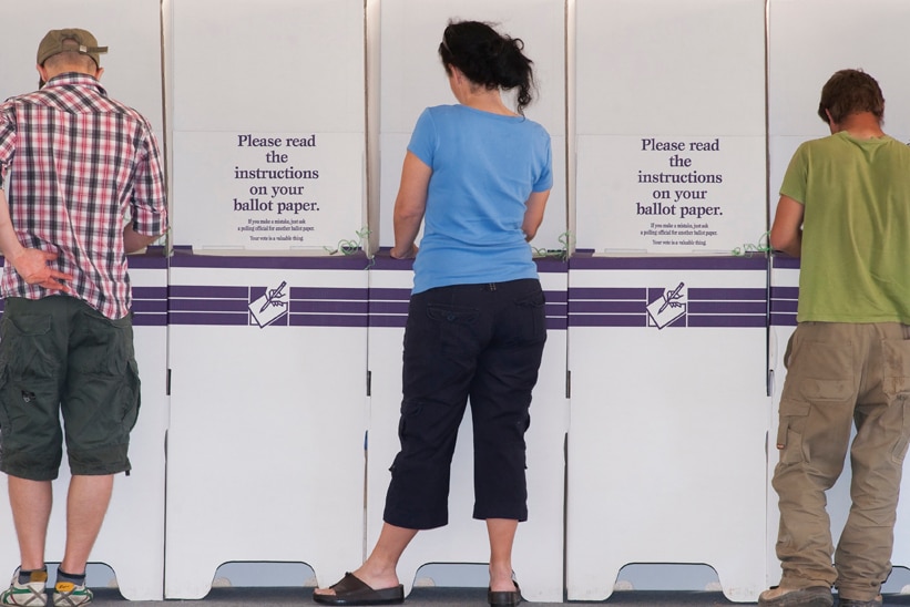 Two men and a woman standing at ballot boxes filling in their ballot papers.