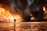 Two children stand on a beach. a cloud of red smoke obscures land from the background