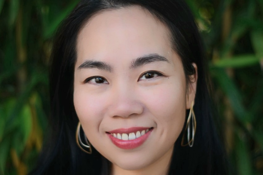 A headshot of a woman with shoulder length black hair wearing grey blazer.