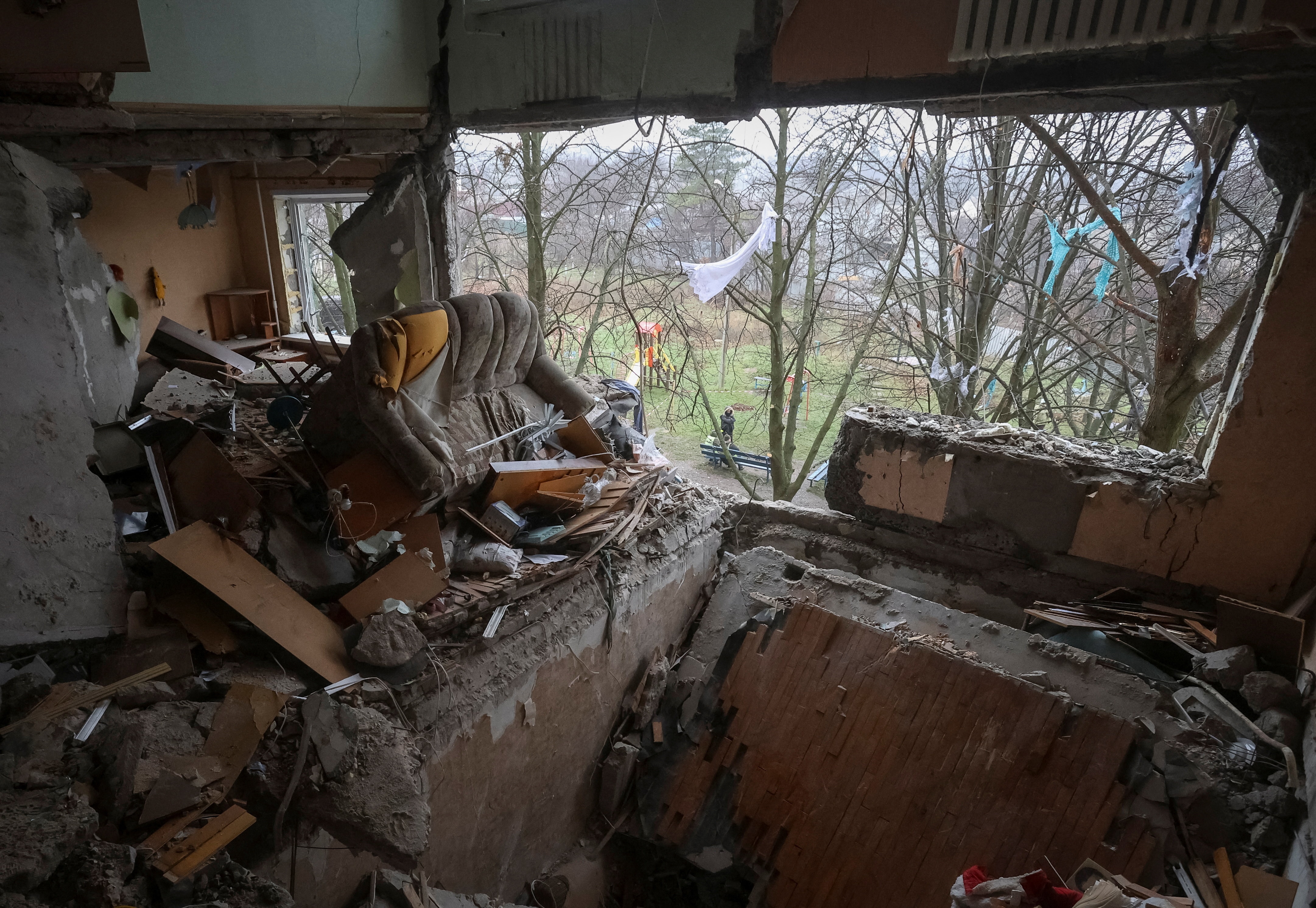 An apartment is destroyed after an explosion inside knocked out the floor and wall overlooking a green area with trees