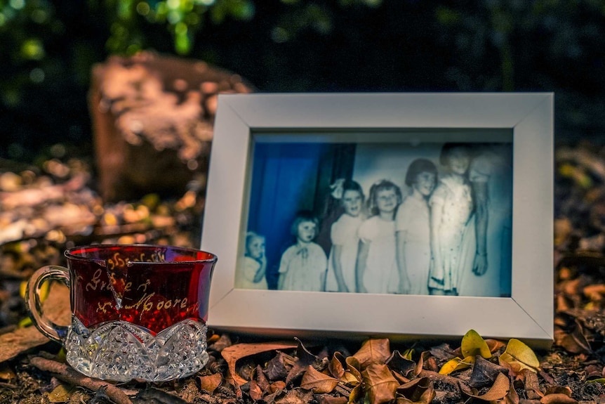 An old framed photograph of seven girls lined up for a photo rests next to a chipped red cup with the name Grace Moore inscribed