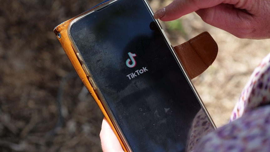 A woman holding a phone with the black and white TikTok logo on the screen.