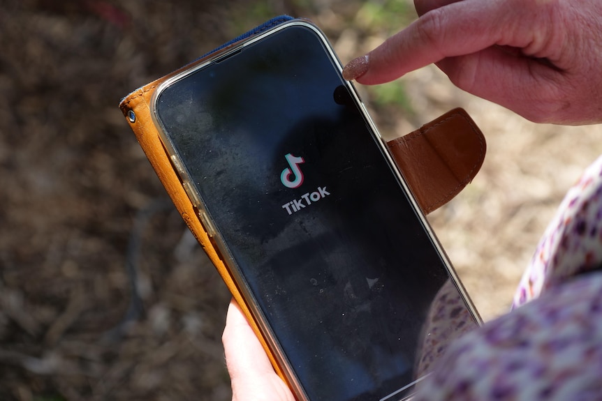 A woman holding a phone with the black and white TikTok logo on the screen